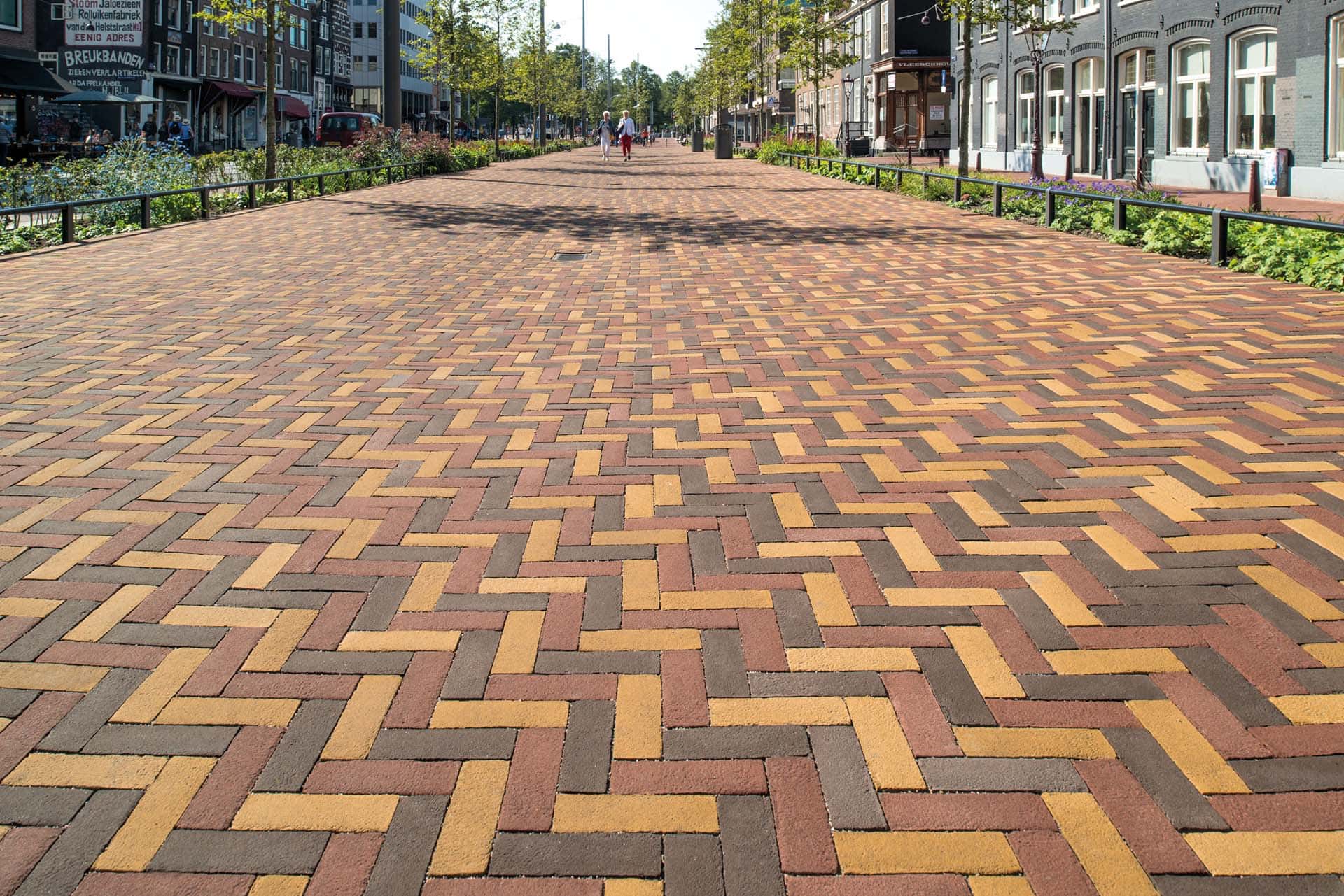 Breiter Fußweg gepflastert mit mehrfarbigen Klinkersteinen Vandersanden in einem herringbone Muster, mit Stadtszenerie im Hintergrund