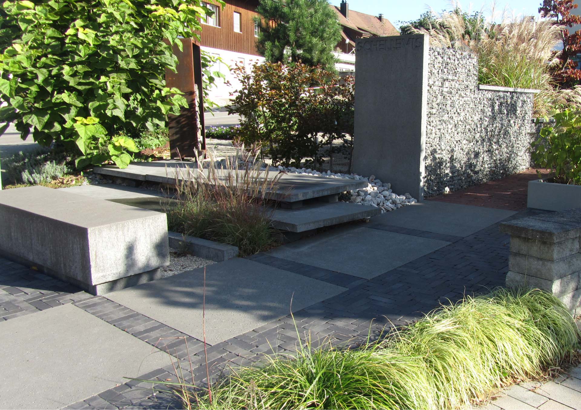 Moderne Gartenideen mit Betonstufen, Gabionenwand, grauen Pflastersteinen und grünen Pflanzenarrangements